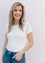 Model wearing jeans with a short sleeve ivory bodysuit with a double clasp closure and a crew neck.