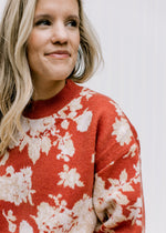 Close up of ivory floral pattern on a brick sweater with long sleeves and a round neck. 