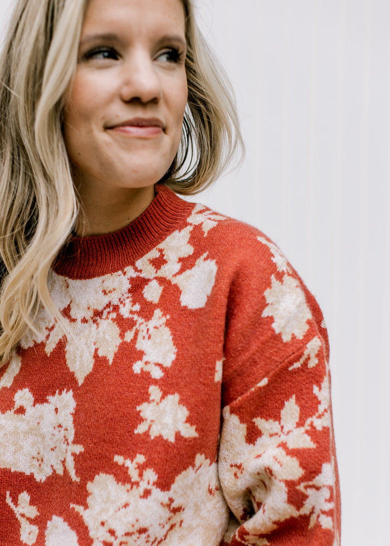 Close up of ivory floral pattern on a brick sweater with long sleeves and a round neck. 