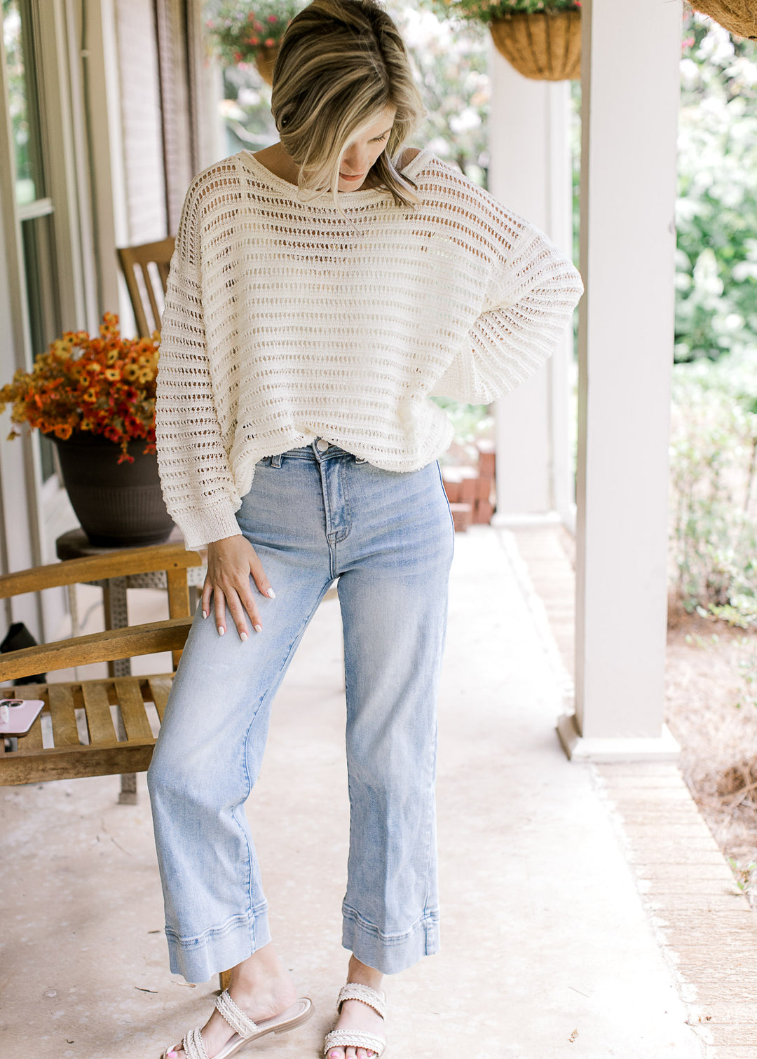 Model wearing jeans, sandals and an ivory open knit blouse with long sleeves and a boat neckline.