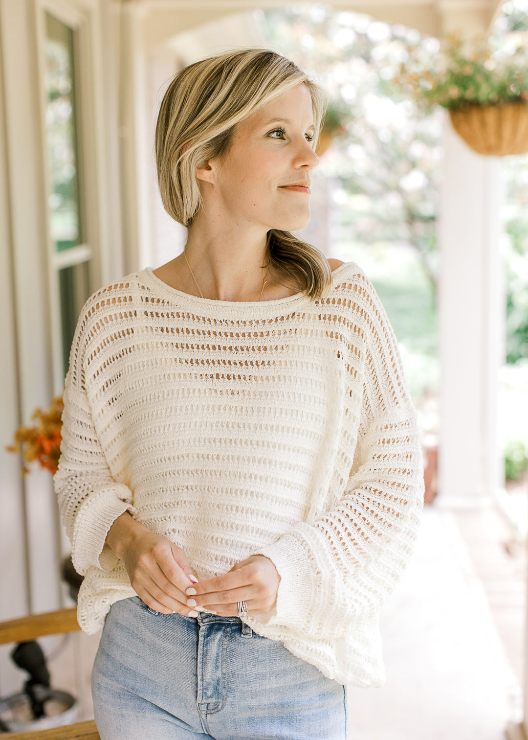 Model wearing an ivory open knit blouse with a weave design, long sleeves and a boat neckline.