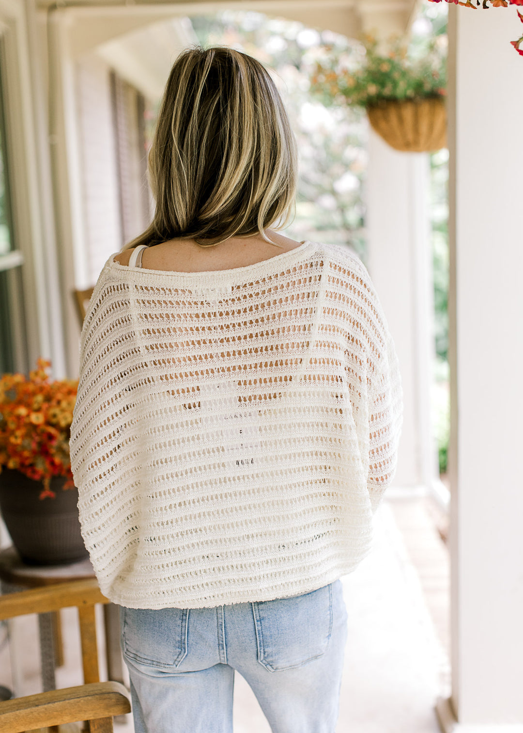 Back view of model wearing jeans and an ivory open knit blouse with long sleeves and a boat neck.