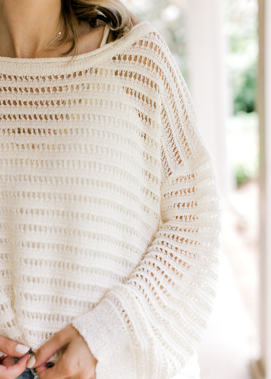 Close up of boatneck and long sleeves on an ivory open knit blouse with a weave design. 