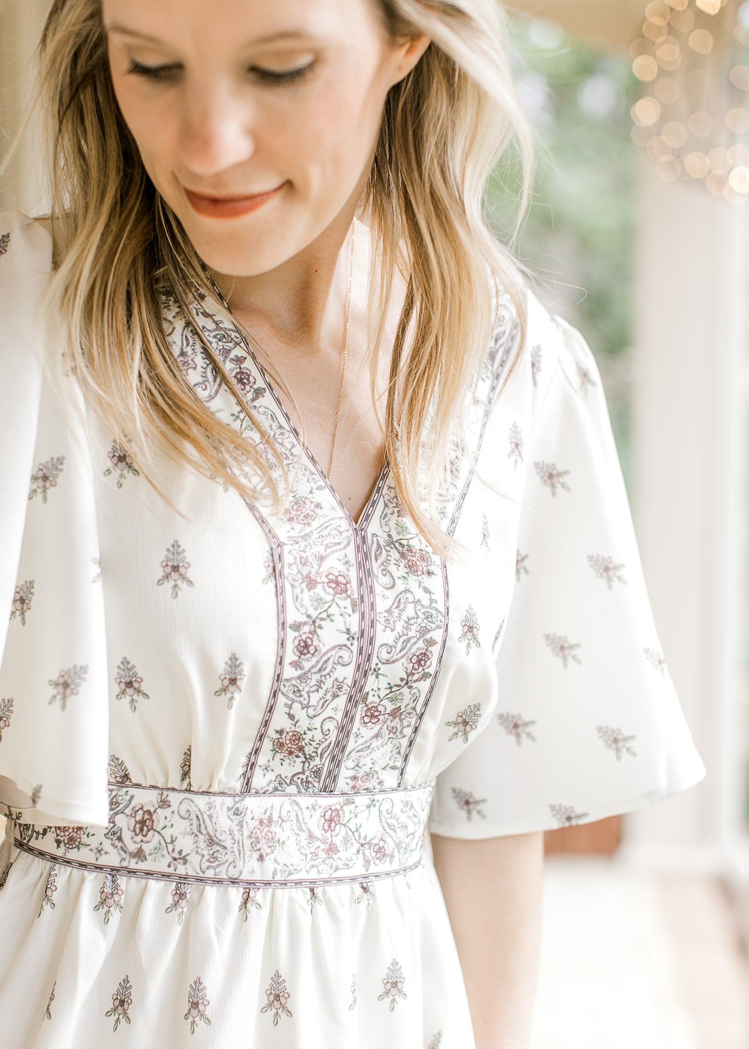 Close up of detail trim at  v-neck bodice, waist, and hem of a short sleeve ivory dress. 