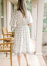 Back view of Model wearing a pale cream dress with mauve and green floral and short sleeves.