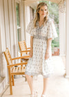 Model wearing a knee length pale cream dress with mauve and green floral, short sleeves and v-neck.