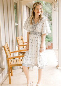 Model wearing a knee length pale cream dress with mauve and green floral, short sleeves and v-neck.