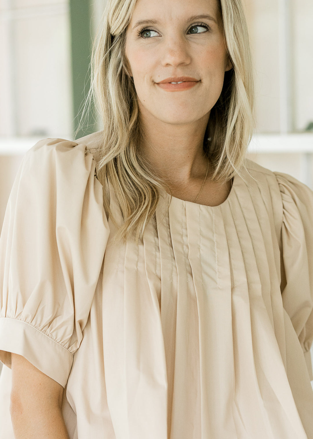 Close up of pleating at neck and shoulder of an ivory top with bubble short sleeves. 