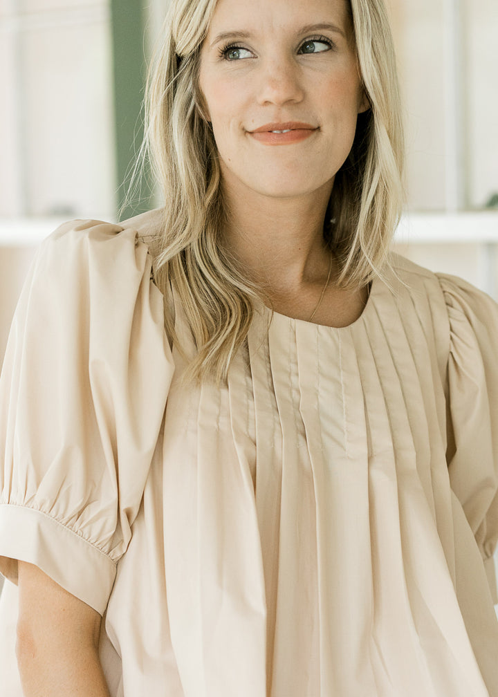 Close up of pleating at neck and shoulder of an ivory top with bubble short sleeves. 