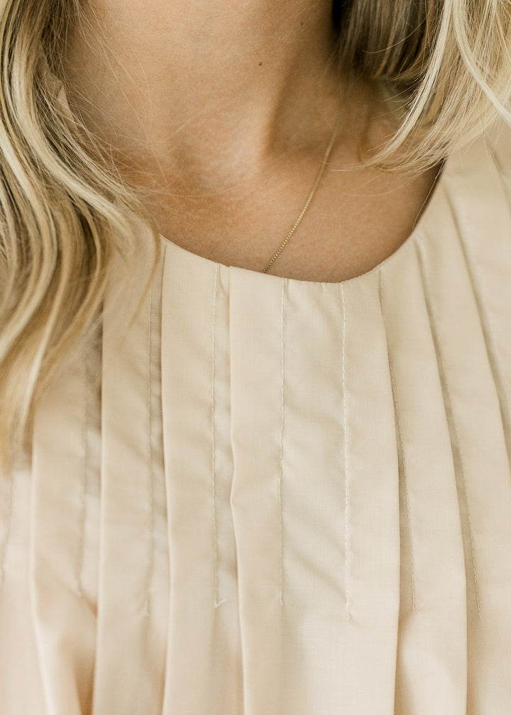 Detail view of round neck and pleating on an ivory top with bubble short sleeves. 