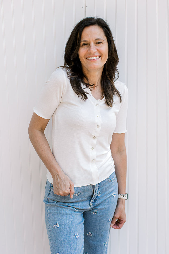 Model wearing a ribbed ivory top with faux pearl buttons, v-neck and short sleeves.
