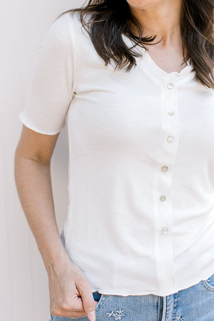 Close up of ribbed material and faux pearl buttons on an ivory top with a v-neck and short sleeves.