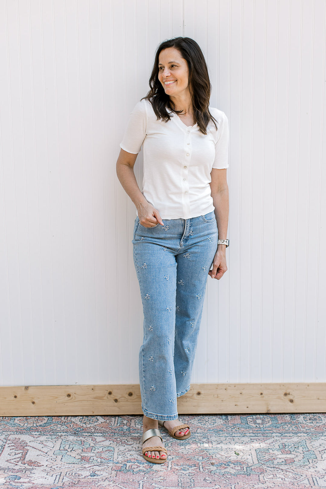 Model wearing jeans and a ribbed ivory top with faux pearl button front, v-neck and short sleeves.