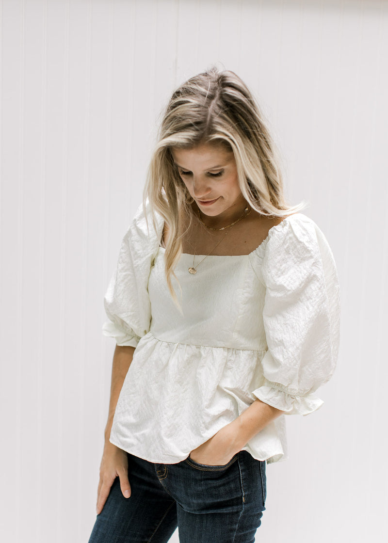 Model wearing an ivory top with a textured material, square neckline and bubble 3/4 sleeves. 