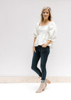 Model wearing jeans and booties with an ivory top with a square neckline and bubble 3/4 sleeves.