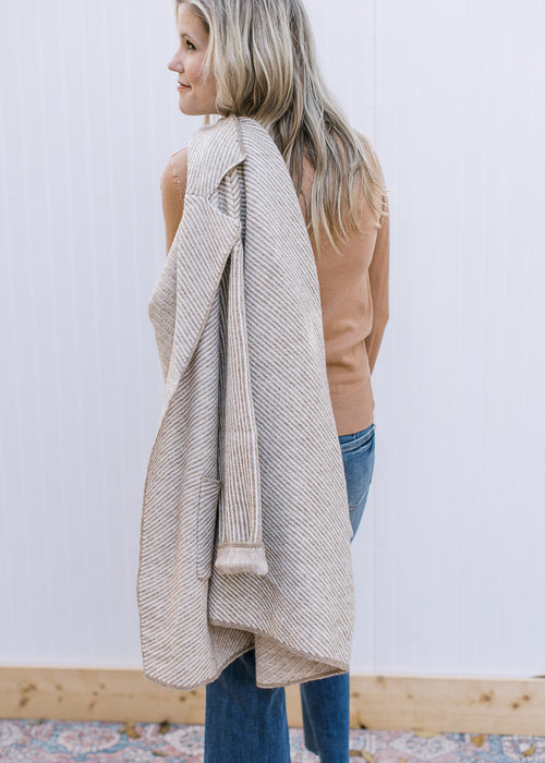 Model holding an ivory open front jacket with tan stripes, patch pockets and long sleeves. 