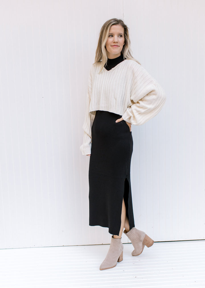Model wearing a ribbed ivory v-neck sweater with a cropped fit and long sleeves with a black maxi..