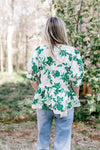 Back view of Model wearing a white short sleeve top with green foliage, v-neck and a peplum fit.