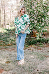 Model wearing jeans and a white short sleeve top with green foliage, v-neck and a peplum fit.