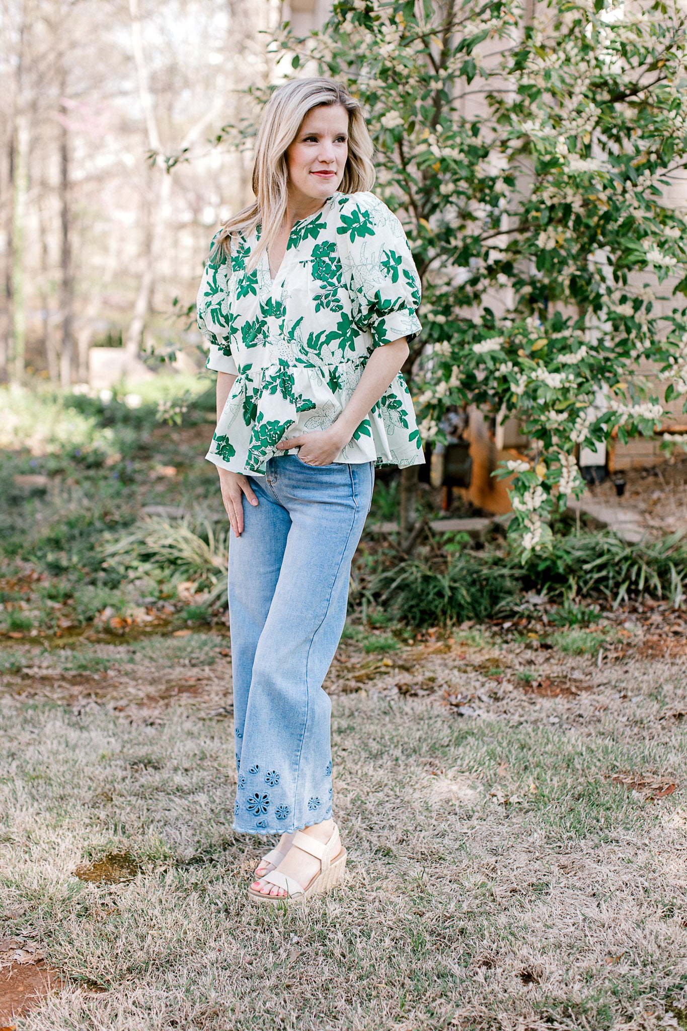 Model wearing jeans and a white short sleeve top with green foliage, v-neck and a peplum fit.