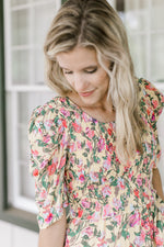 Close up of smocked bodice and short sleeves on a yellow dress with a pink and green floral. 