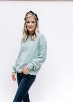 Model wearing a cozy jade knit top with a round neck, long sleeves and rolled hem detail. 