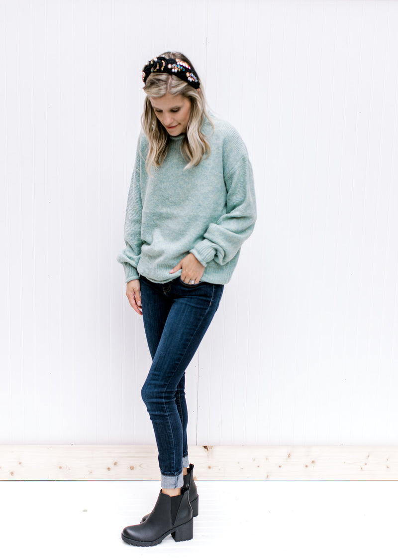 Model wearing a black headband and jeans with a jade top with long sleeves and rolled hem detail. 