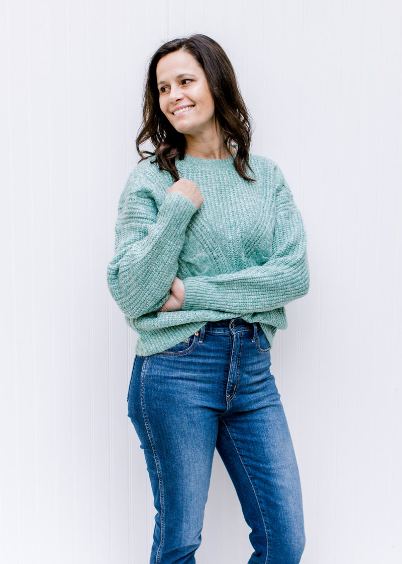 Model wearing a jade sweater with cable knit fabric, long sleeves and a round neckline. 