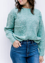 Model wearing a cozy jade sweater with cable knit fabric, long sleeves and a round neckline. 