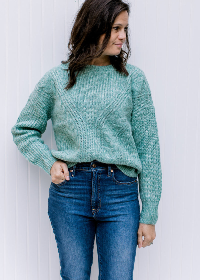 Model wearing jeans with a jade sweater with cable knit fabric, long sleeves and a round neckline. 