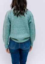 Back view of Model wearing a jade sweater with cable knit fabric, long sleeves and a round neck. 