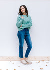 Model wearing jeans and mules with a jade cable knit sweater with long sleeves and a round neckline.