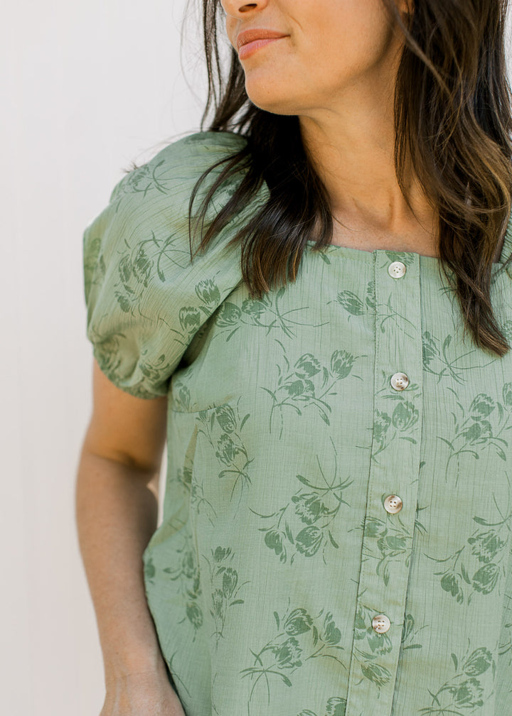 Model wearing a sage top with floral, button down front square neck and short sleeves.