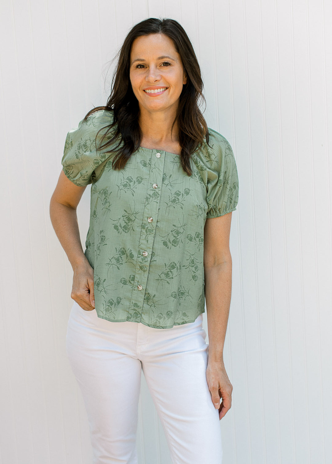 Model wearing a sage top with floral, button front, square neck and bubble short sleeves.