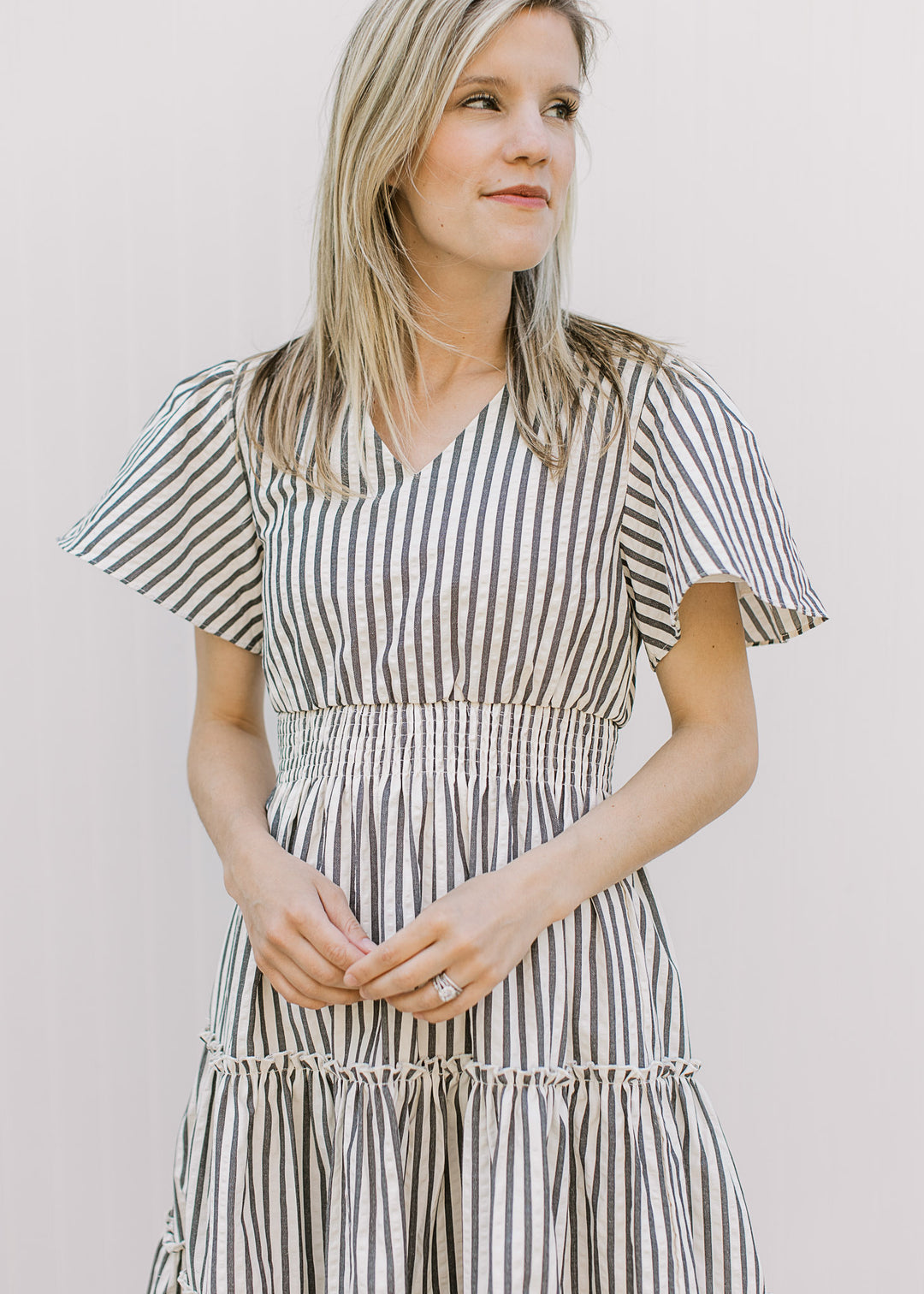 Model wearing an off-white knee length dress with charcoal stripes, v-neck and short sleeves.