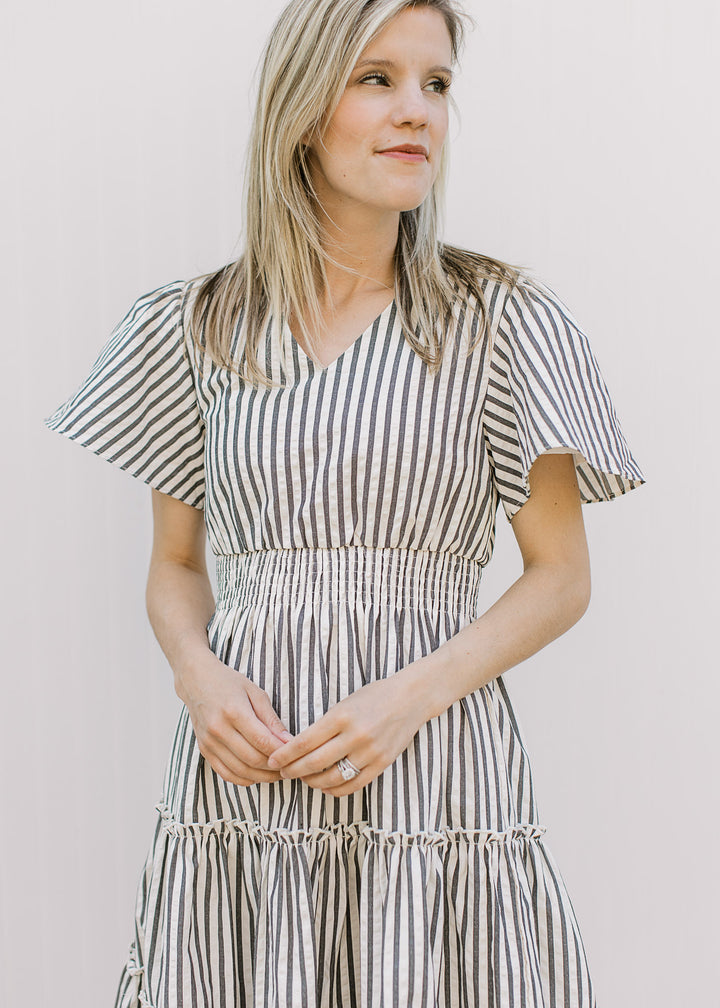 Model wearing an off-white knee length dress with charcoal stripes, v-neck and short sleeves.