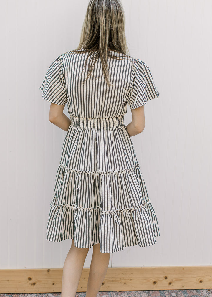 Back view of Model wearing an off-white dress with charcoal stripes, v-neck and short sleeves.