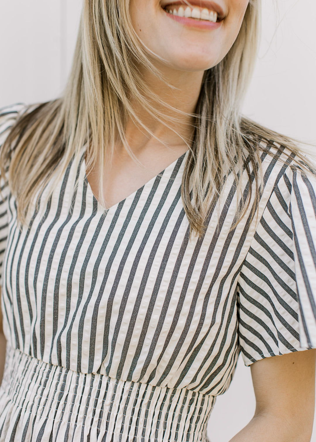 Close up of v-neck, flutter short sleeves and elastic waist on a cream and charcoal striped dress.