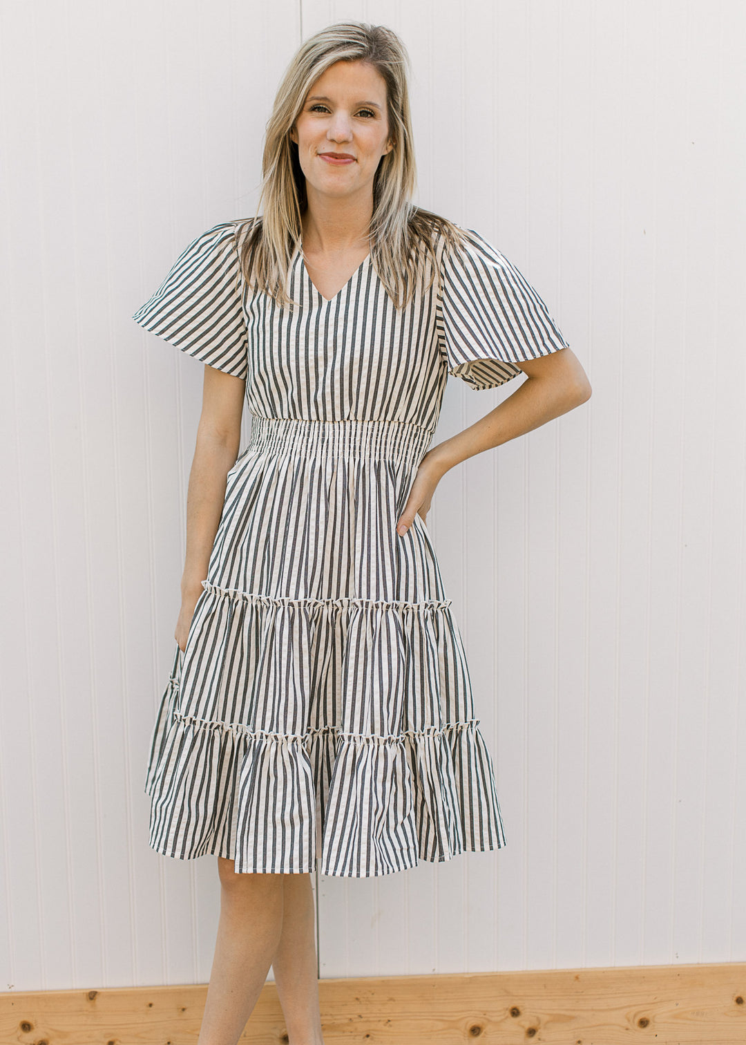 Model wearing an off-white dress with charcoal stripes, elastic waist, v-neck and short sleeves.