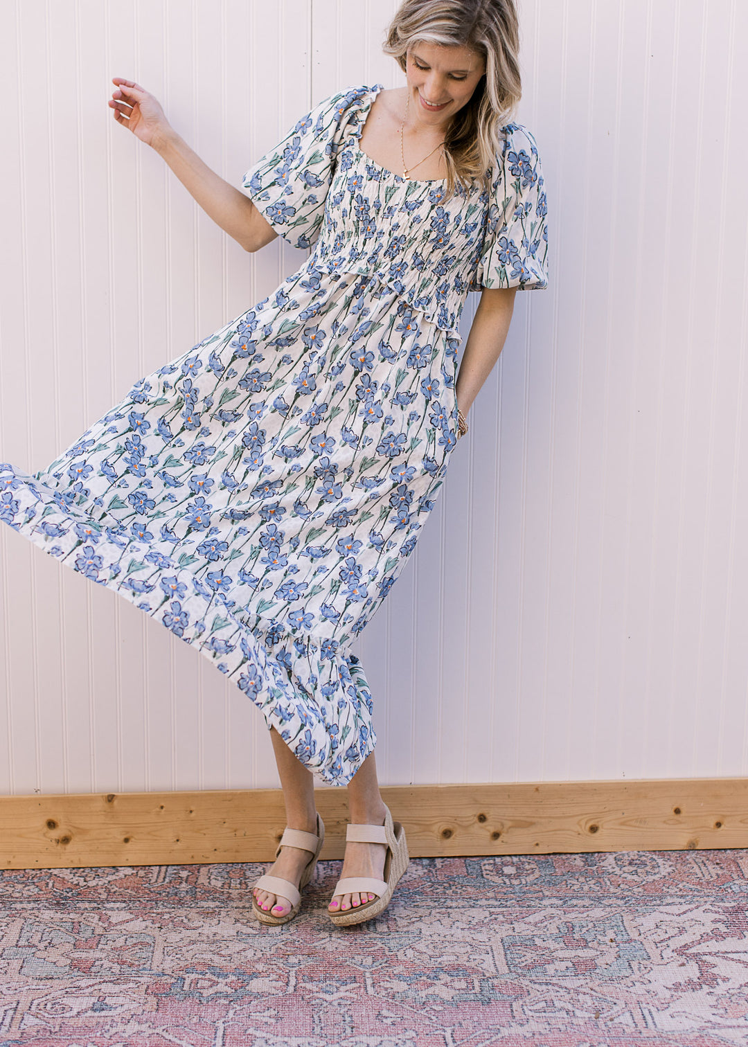 Model twirling an off-white midi with blue floral, a smocked bodice and bubble short sleeves. 