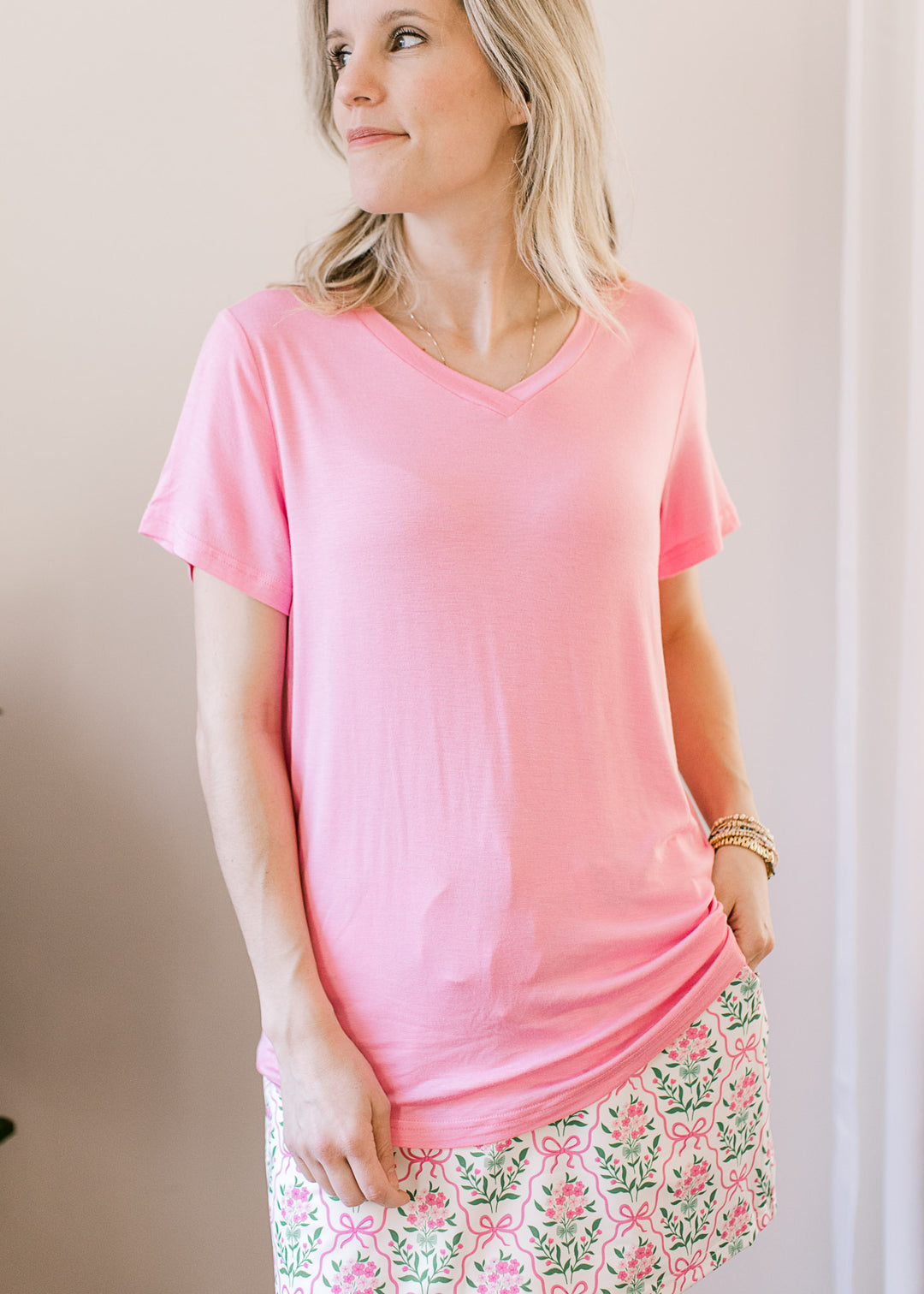 Model wearing a soft pink top with a v-neck, short sleeves and a lightweight, stretchy fabric.
