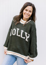 Model wearing a hunter green sweater with “JOLLY” across the front in cream font and long sleeves.