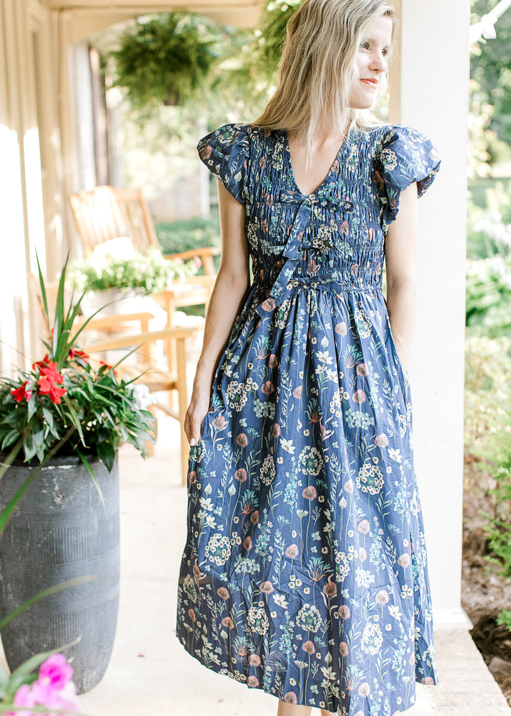 Model wearing a blue midi with bright floral, smocked bodice and bubble short sleeves. 