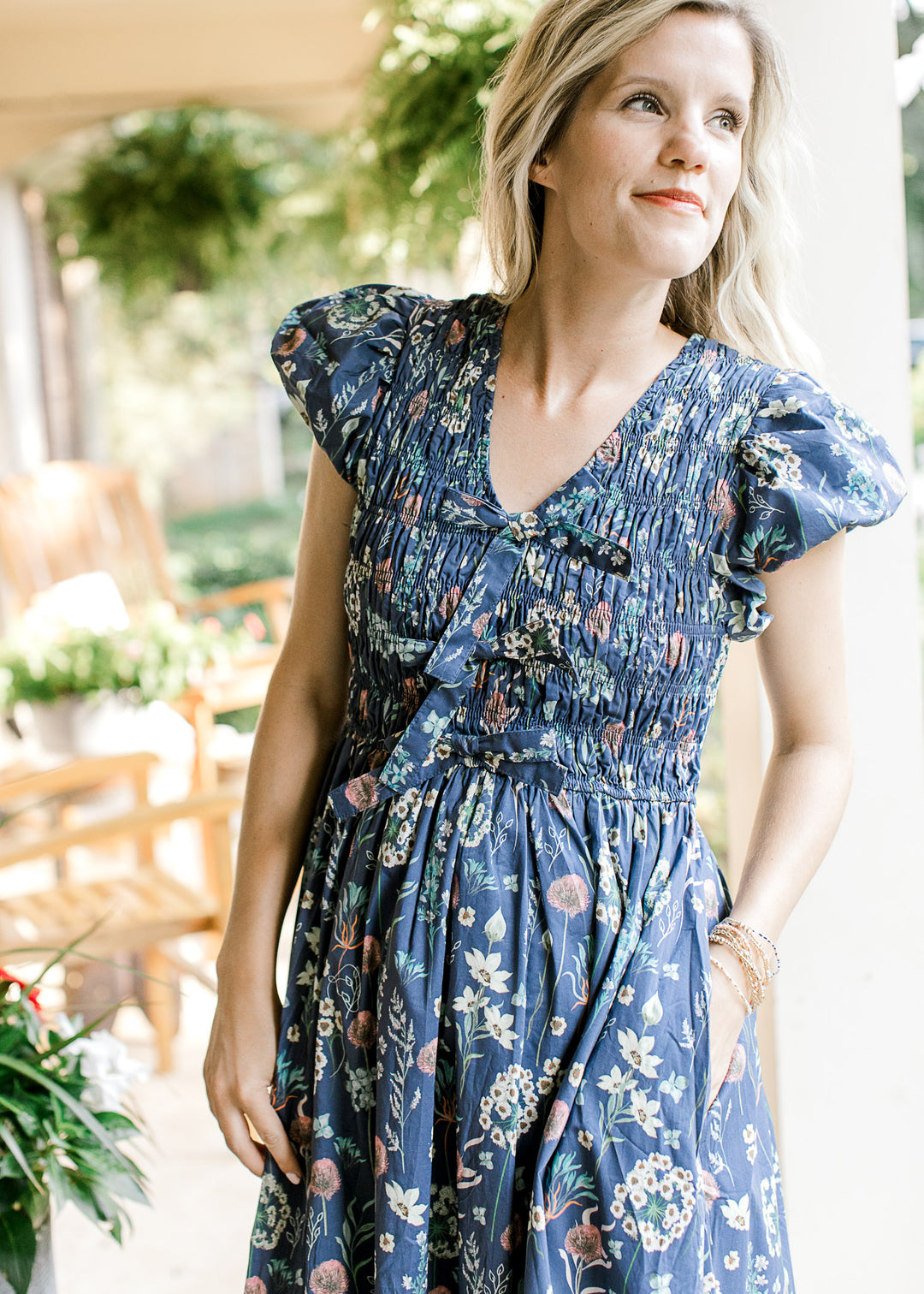 Model wearing a blue midi with bright floral and smocked bodice with three faux bows. 