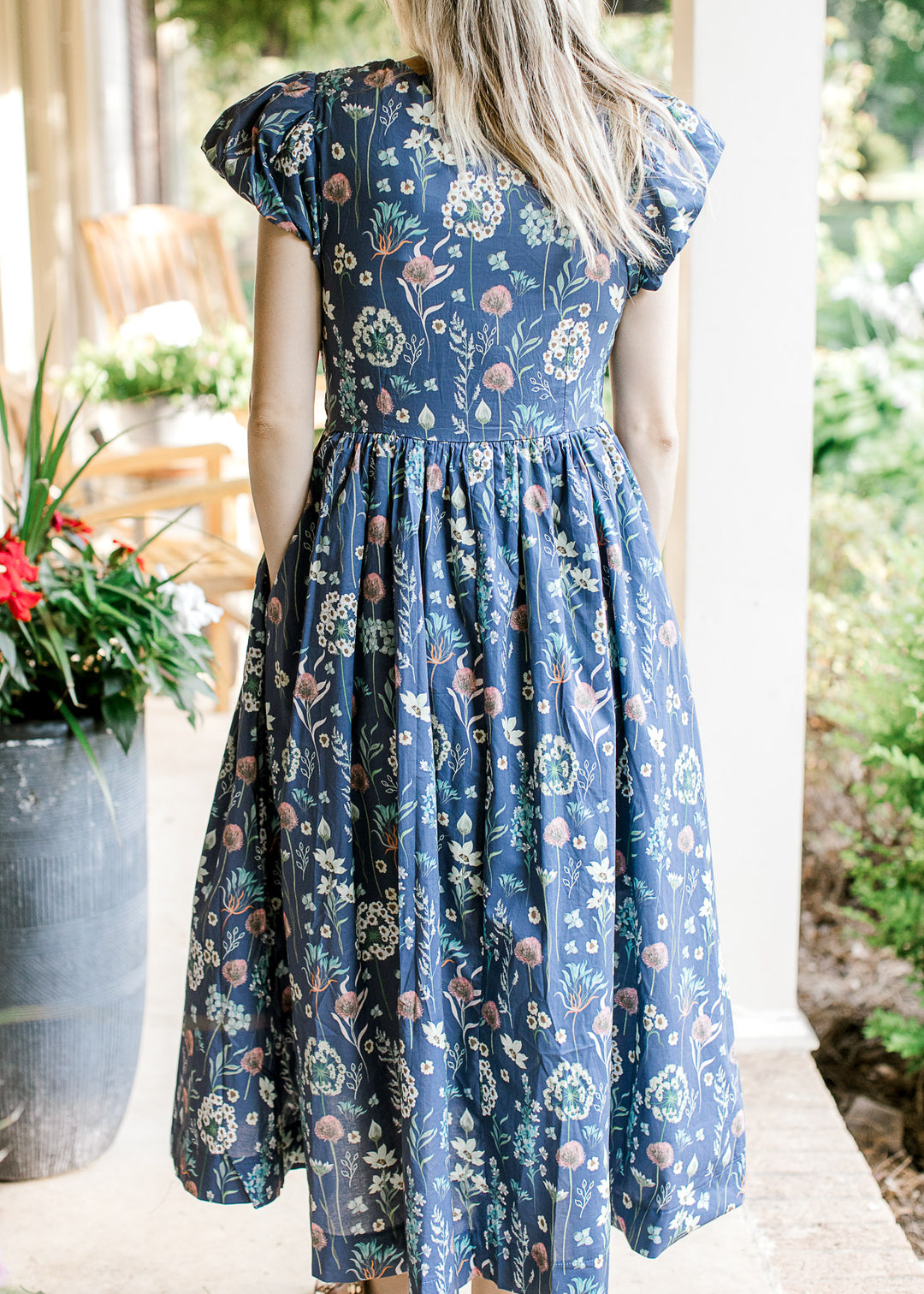 Back view of Model wearing a blue midi with bright floral and bubble short sleeves. 