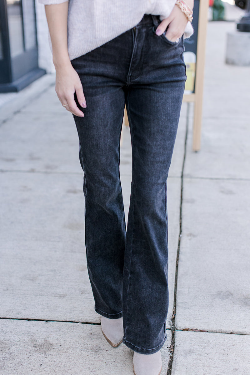 Model wearing a cream top, booties and black jeans with tummy control, high waist and bootcut fit. 