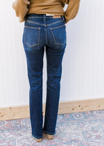 Back view of model wearing mid rise, dark wash jeans with a boot cut and stretchy fit. 