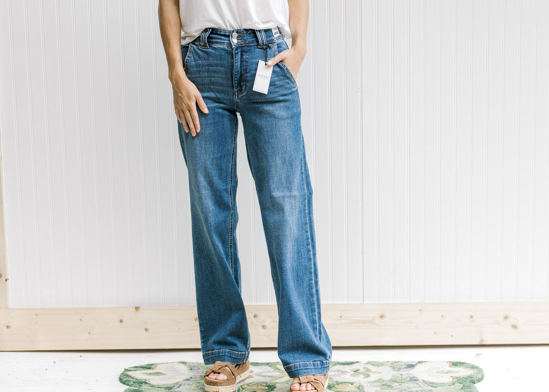 Model wearing a white top, wedges and medium wash wide leg jeans with a double button closure. 
