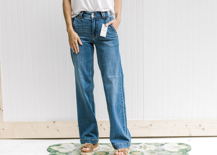 Model wearing a white top, wedges and medium wash wide leg jeans with a double button closure. 