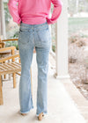Back view of Model wearing medium washed boot cut jeans with frayed hem and high waisted fit. 